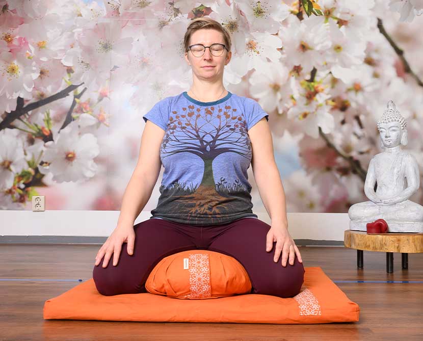A female meditating sitting on the orange Zafu meditation cushion and Zabuton mat