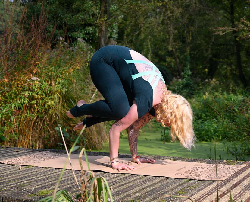 A female in green jumpsuit is practicing Kakasana (Crow Pose)