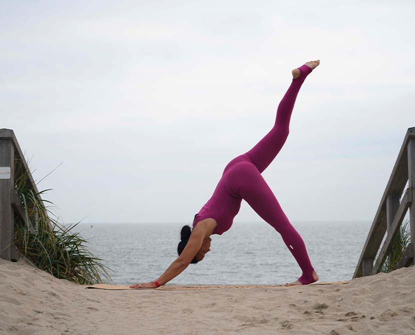 Female in red jumpsuit doing arm balance on the beach